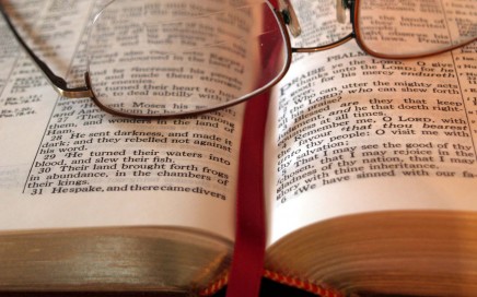 The middle of an open Bible with reading glasses set down upon it