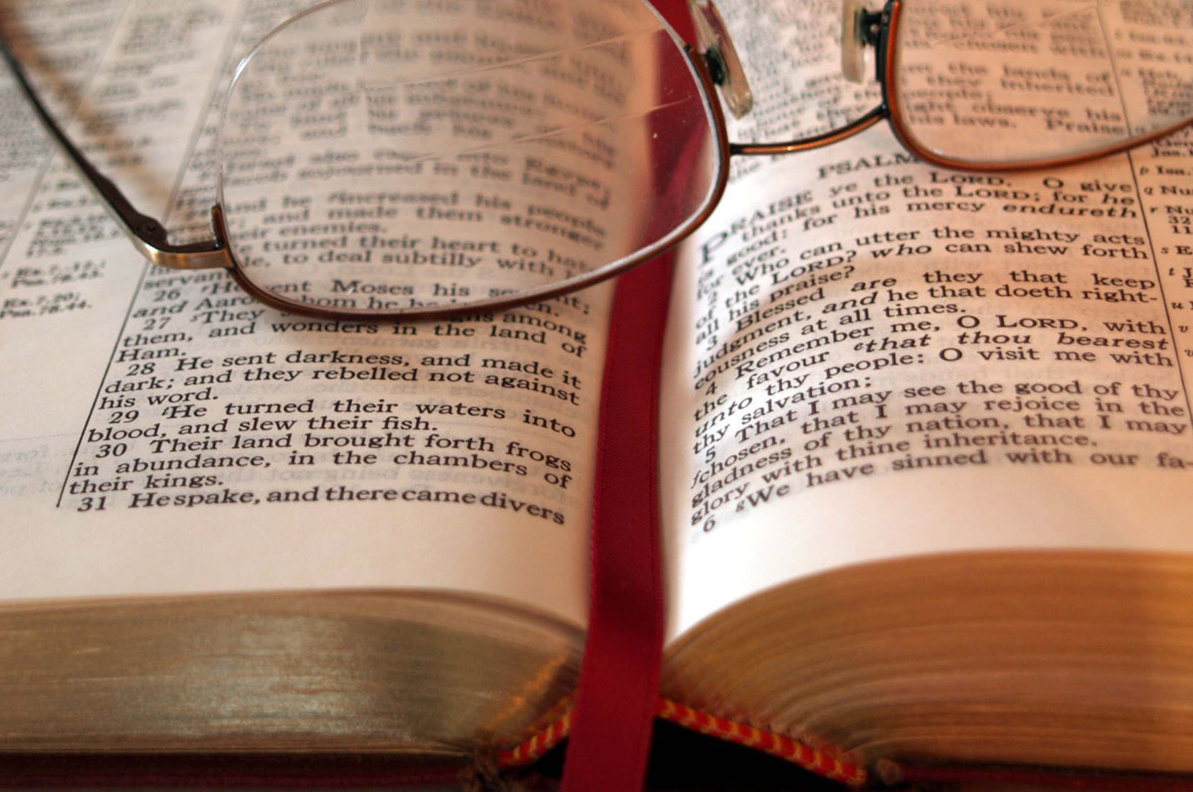 The middle of an open Bible with reading glasses set down upon it