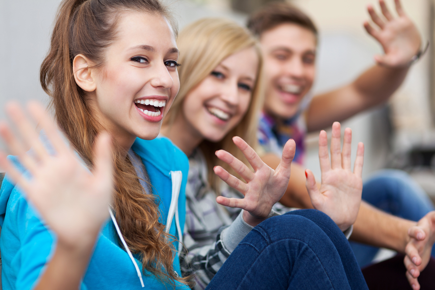 three teenagers smiling and waving